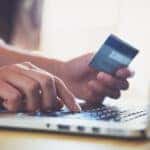 Hand holding credit card beside laptop