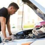 Profile view of a handsome young Hispanic man looking at a car with its hood open, trying to fix it