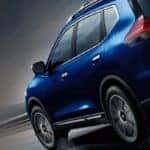 Blue 2019 Nissan Rogue from behind driving against black background