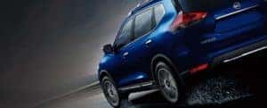 Blue 2019 Nissan Rogue from behind driving against black background