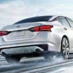 White 2020 Nissan Altima driving on snowy mountain road toward city