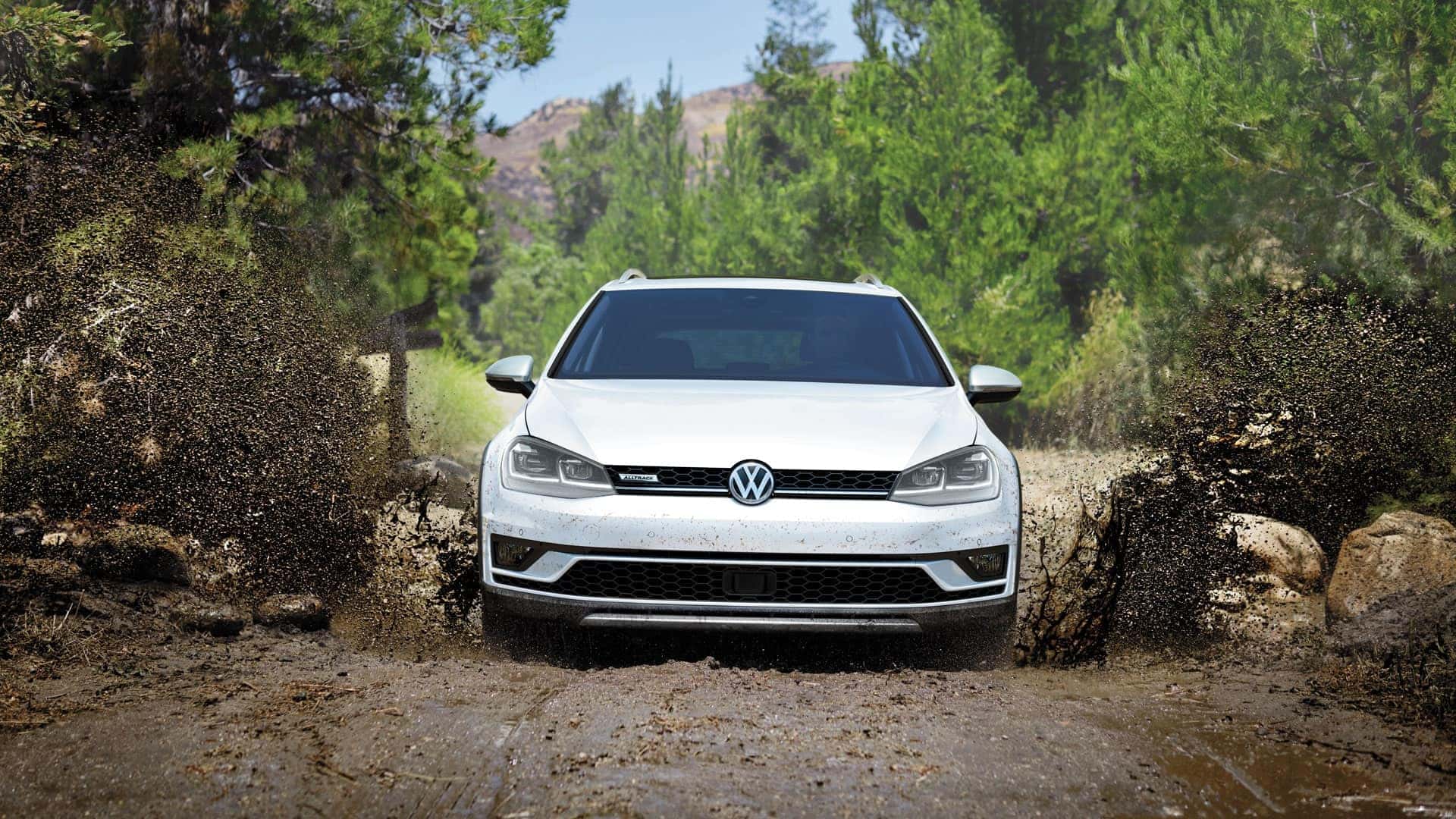 White 2019 VW Golf Alltrack offroading through a giant puddle of mud.