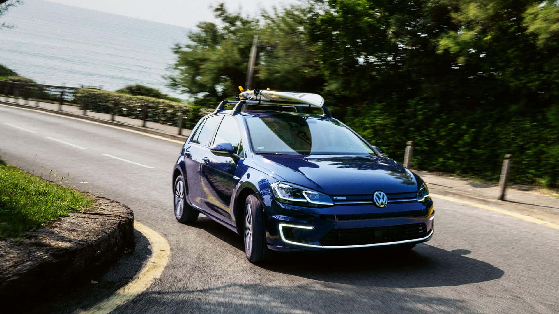 Blue 2019 VW e-Golf turning a corner. A surf board is on the roof rack.