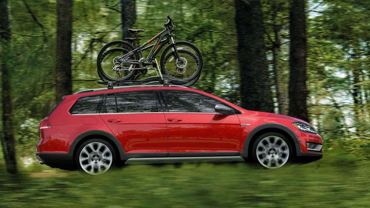 Red 2019 VW Golf Alltrack driving through a forest with bikes on the roof rack