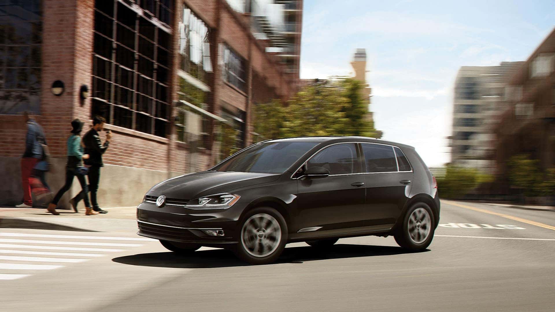 A black 2019 VW Golf showing off it's cross differential system to several hipsters outside an old factory that has been converted to office space or lofts.
