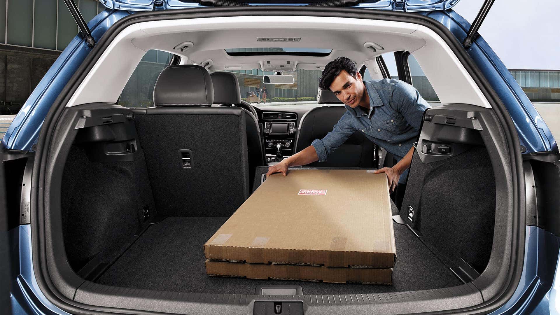 Man using the 2019 VW Golf folding seats feature to transport otherwise unwieldy boxes.