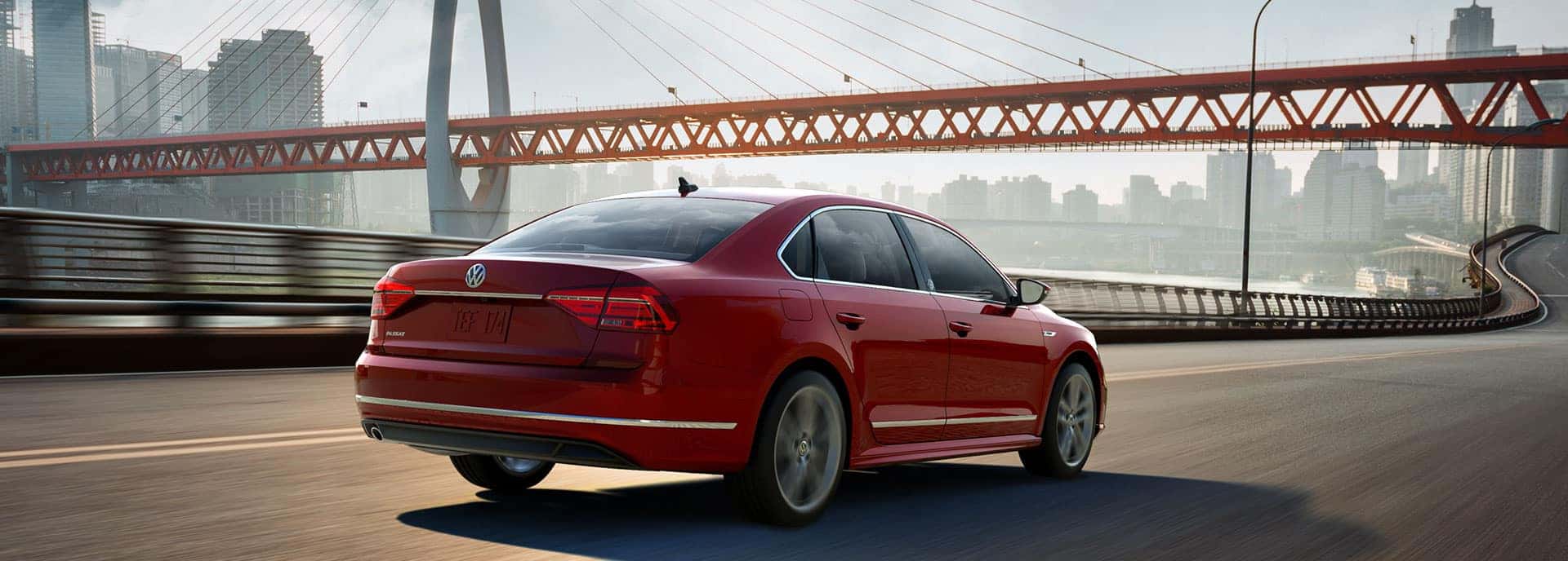 2019 VW Passat driving on a winding, urban street that passes below a large bridge and overlooks a nearby body of water.