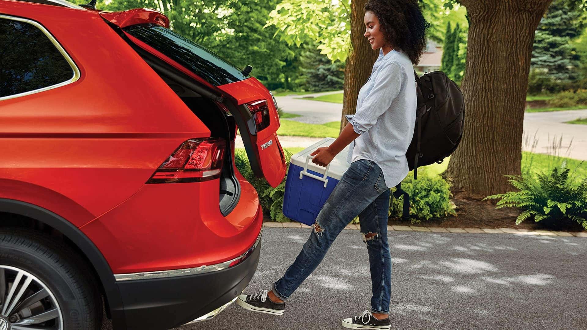 Woman with her hands full takes advantage fo the Tiguan's power liftgate by simply waving her foot under the rear bumper to open the rear door.